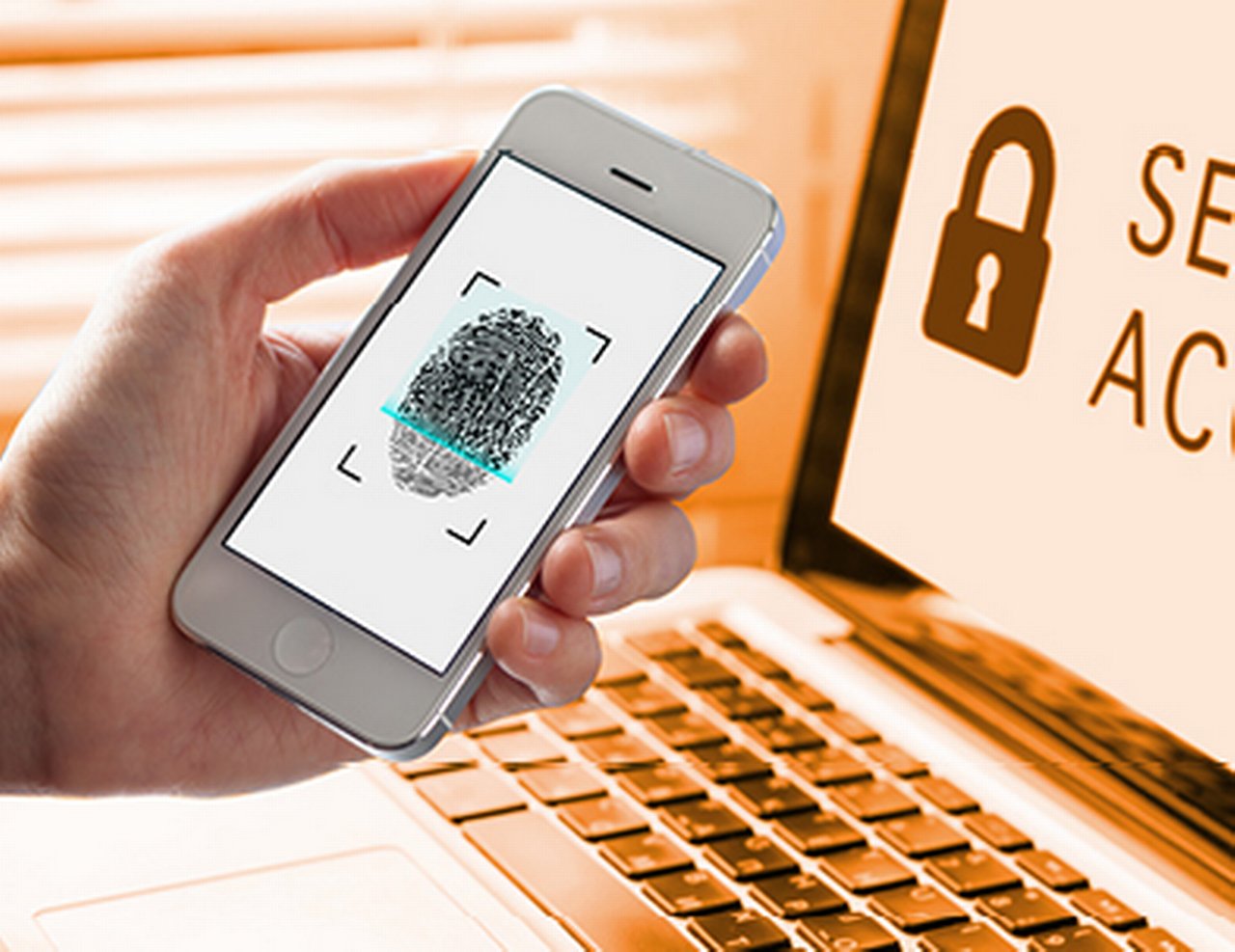 Hand holds up a smartphone in front of a laptop, showing a fingerprint scan.