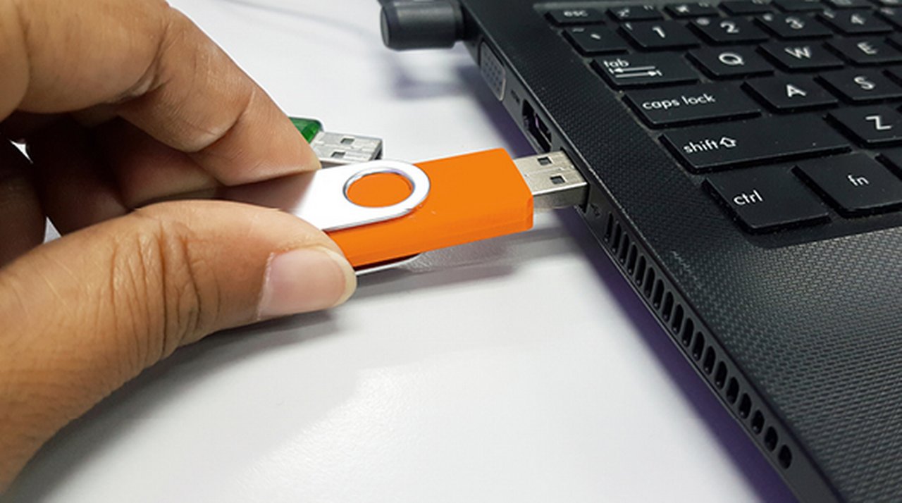 Hand steckt einen USB-Stick seitlich in einen Laptop