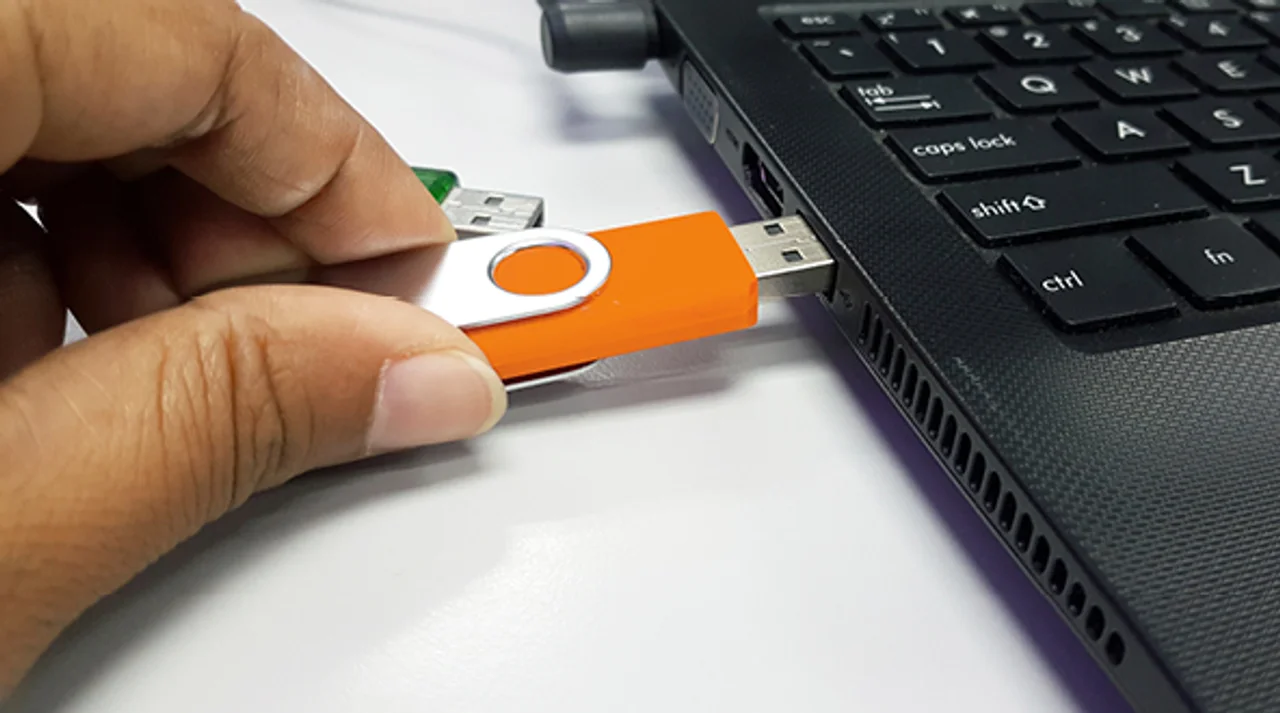 Hand inserts a USB stick into the side of a laptop
