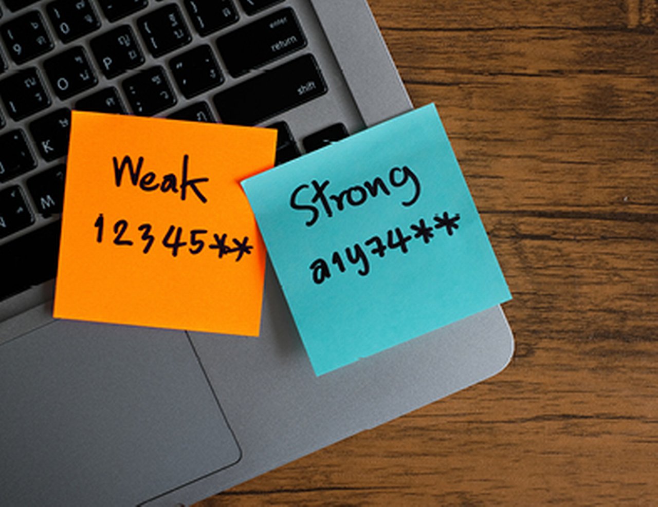 Two sticky notes on a laptop keyboard, one with a weak password and one with a strong password