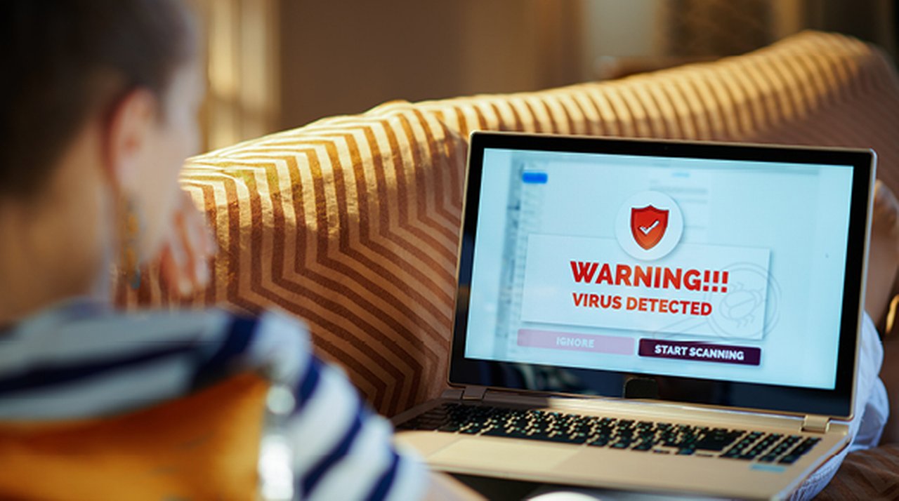 Laptop, dessen Bildschirm eine Warnmeldung zeigt, mit einer Frau davor auf einem Sofa