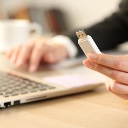 Hand hält einen USB-Stick neben einem Laptop