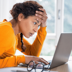 Woman sitting in front of a laptop, touching her face while looking at the screen