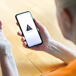 A person holds a smartphone displaying a warning symbol on the screen