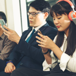 Zwei Pendler nutzen Smartphones, w&auml;hrend eine Person Kopfh&ouml;rer tr&auml;gt