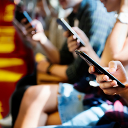 Several people sitting next to each other on a bench, each holding a smartphone and looking at it