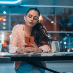 A woman sitting at an airport, holding her smartphone in her hands and looking at it with her elbows on the table