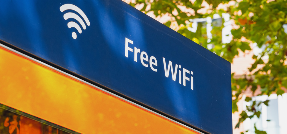 A building wall with a shop sign reading &ldquo;Free WiFi,&rdquo; with tree branches in the background