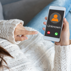 A woman on a sofa holds a smartphone showing an incoming call from an unknown number